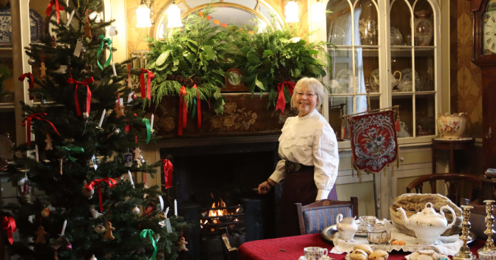 Woman stoof by fireplace inside a 1900s house decorated for Christmas at Beamish Museum.